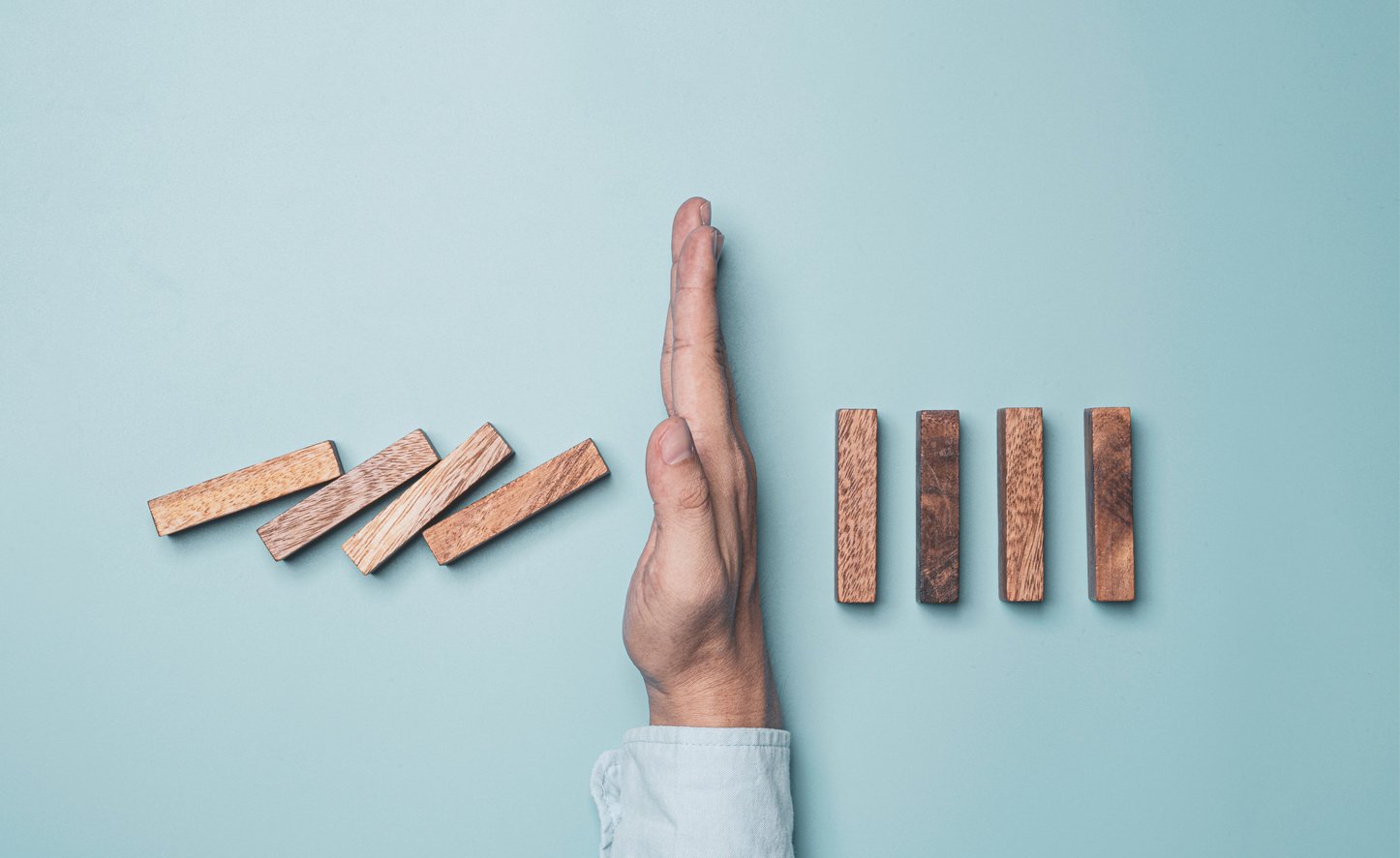 Businessman hand protecting rectangle  block which falling to stop dominos others rectangle standing on blue background. Risk and crisis management concept.